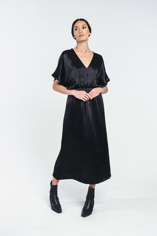 Black midi a-lined dress with o-logo made from recycled viscose.  Rubber band waist and t-shirt sleeves. Worn by a model showing the dress with v-neck on the front. Hálo from north