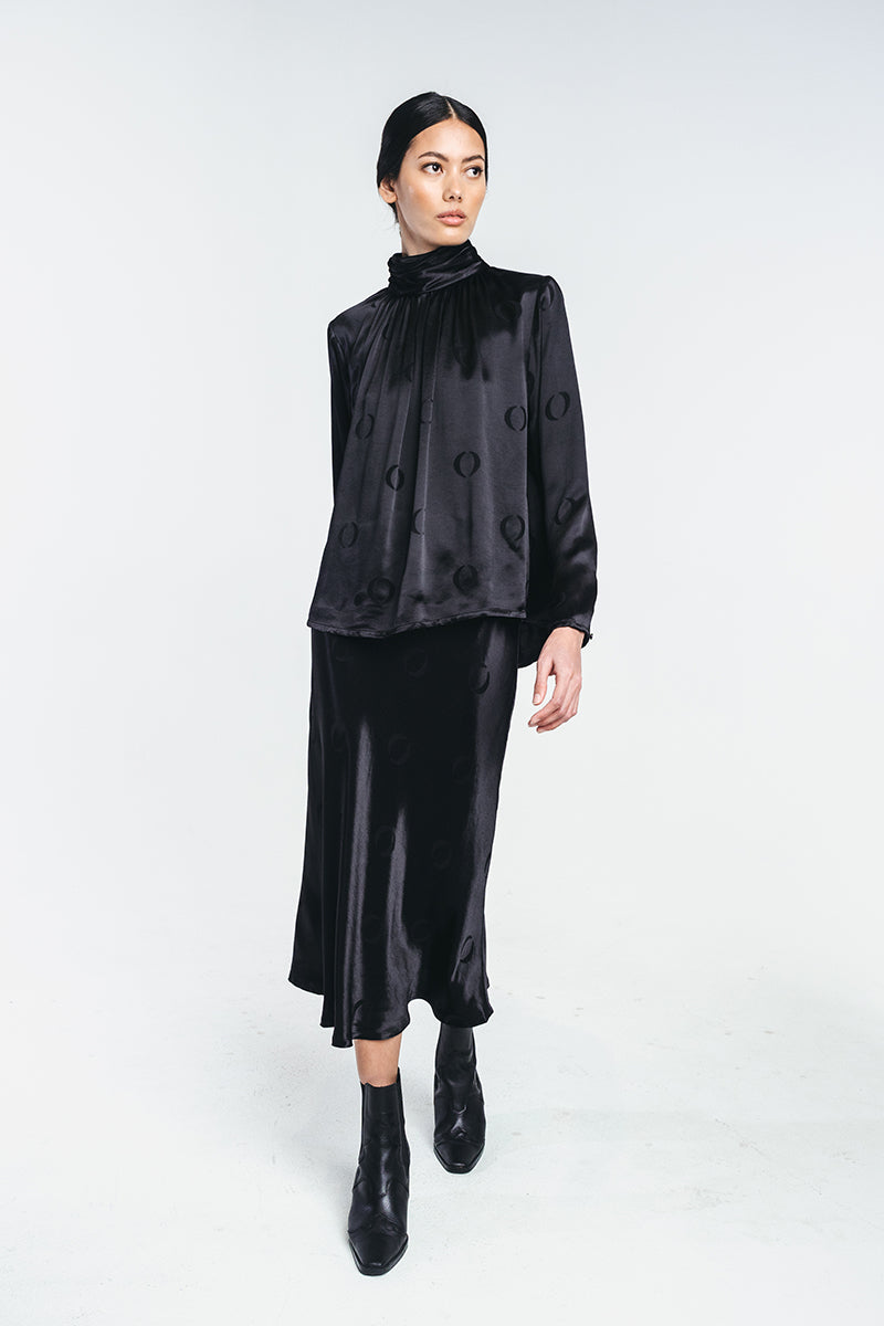 Black viscose shirt with o-logo, wrinkled turtle neck and buttoned sleeves worn by a model with matching o-logo skirt.  Video showing the garment. Made from recycled viscose. Hálo from north