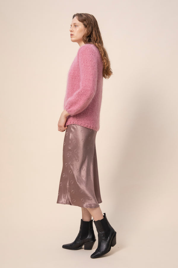 Huurre handknitted wrapknit in mauve worn as a cardigan. Handmade in Italy. Model is wearing the knit, ribbed top and taupe o-logo skirt. Video