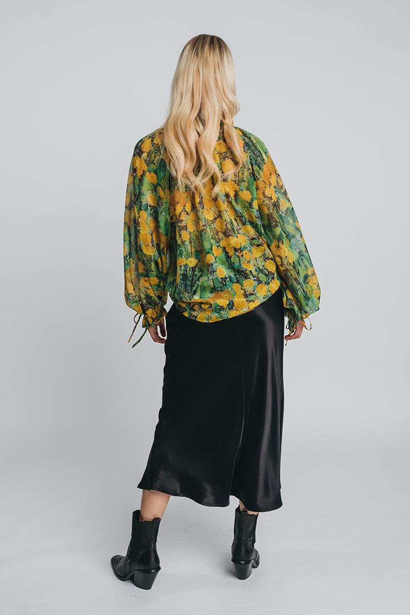 Reidar silk chiffon blouse in green and yellow worn together with kajo slip skirt in black. Picture from behind. Hálo x Reidar Särestöniemi EXCLUSIVE